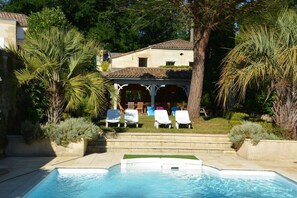 A swimming pool with lounge chairs, a covered seating area, and surrounding greenery.