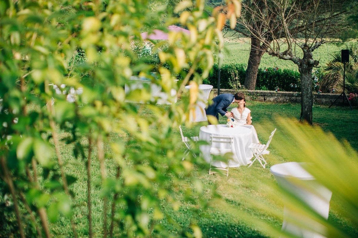 Un lieu de réception en plein air pour les mariages, avec des tables et des chaises rondes, entouré de verdure et d’un arbre.