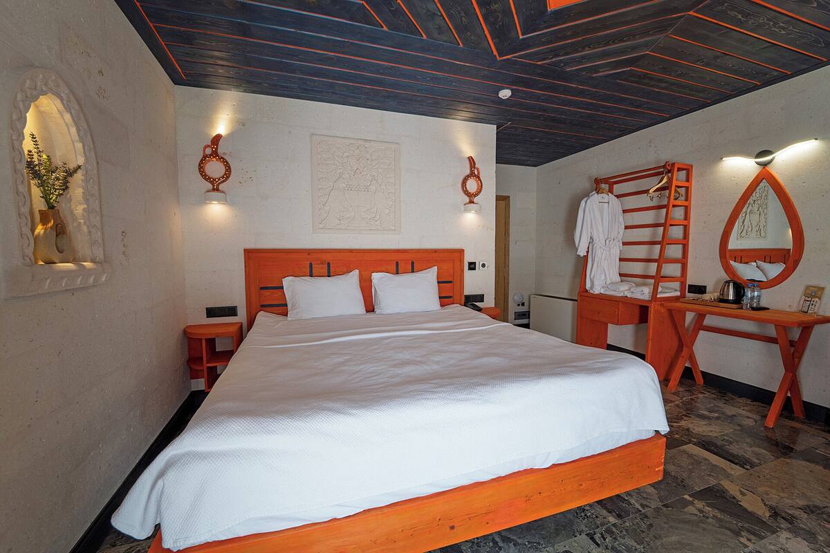 A bedroom with a wooden bed, a wooden desk with a mirror, and a wall-mounted light fixture.
