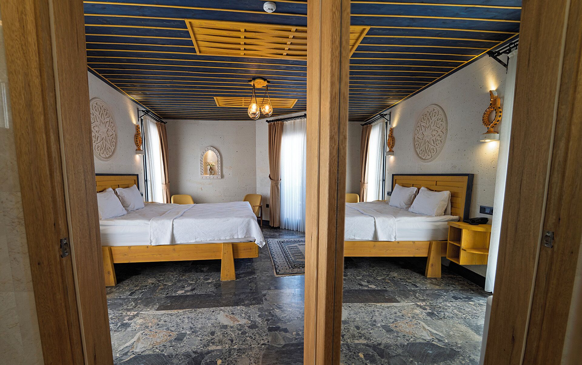 Habitación con espejos, dos camas, techo de madera y piso estampado.
