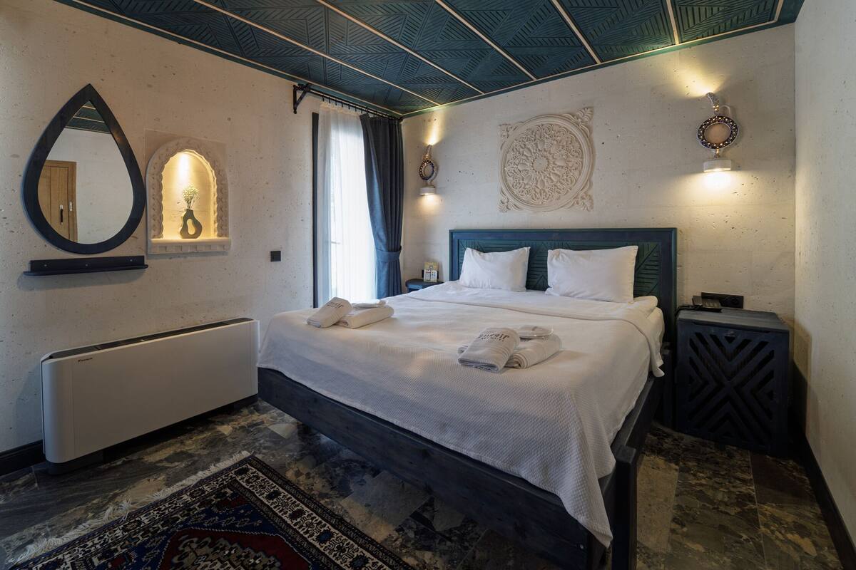 A bedroom with a bed, a bedside table, a wall-mounted mirror, a radiator, and a patterned rug.