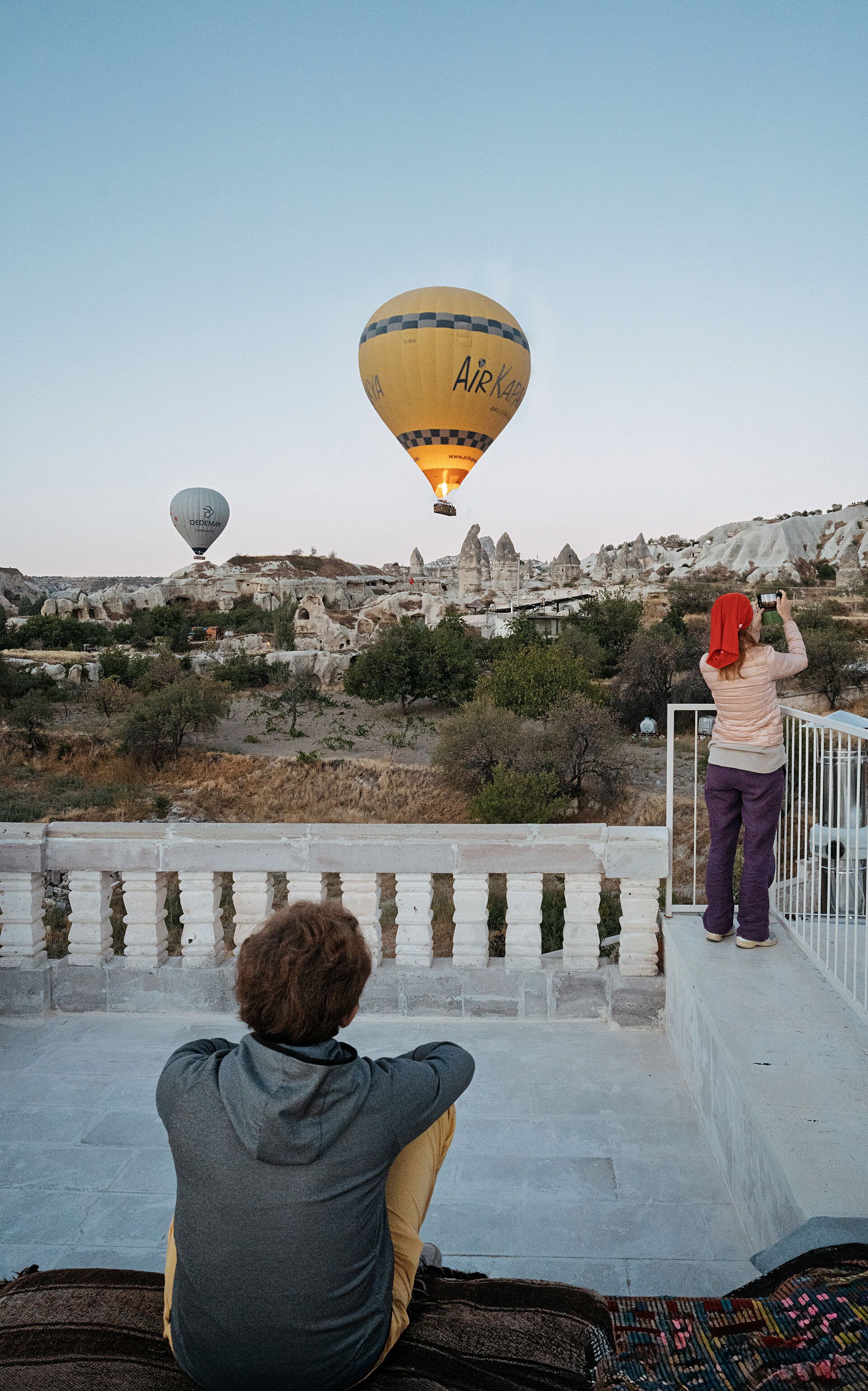 Una persona observa globos aerostáticos sobre un paisaje rocoso con formaciones rocosas singulares.