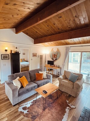Una sala de estar acogedora con techo de madera, un sofá, un sillón, una mesa de centro y un tapiz de cuero de vaca.