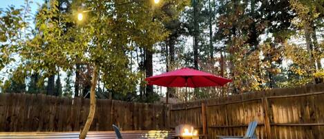 Een terras met twee lounge fauteuils, een rode parasol en een vuurkorf.