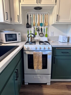 A kitchen with a stove, oven, microwave, and various utensils hanging on the wall.