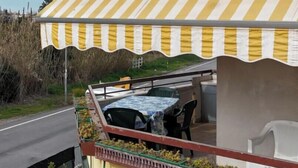 A building with a yellow and white striped awning, a balcony with a table and chairs, and a view of a road and vegetation. - M383 - Marcelli, comfortable three-room apartment 200mt from the sea (Marcelli)