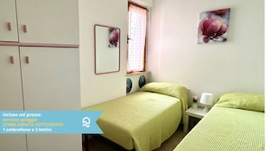 A bedroom with two beds, a window with a curtain, a bedside table with a lamp, and a wall-mounted mirror. - M383 - Marcelli, comfortable three-room apartment 200mt from the sea (Marcelli)