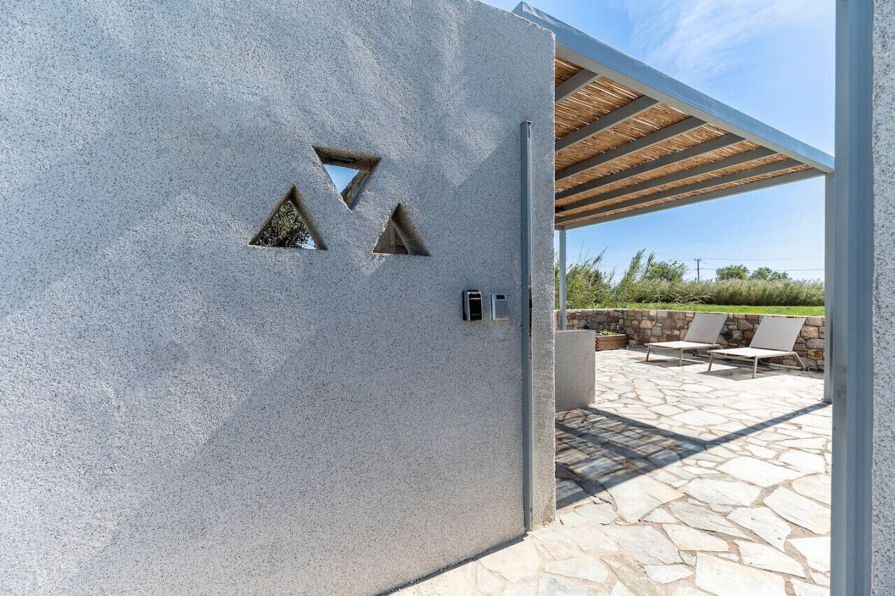 Un edificio moderno con facciata strutturata, una pergola in legno, pavimento in pietra e area salotto esterna.