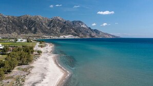 Paesaggio costiero con spiaggia limpida, catena montuosa sullo sfondo e piccolo insediamento con edifici vicino alla riva.