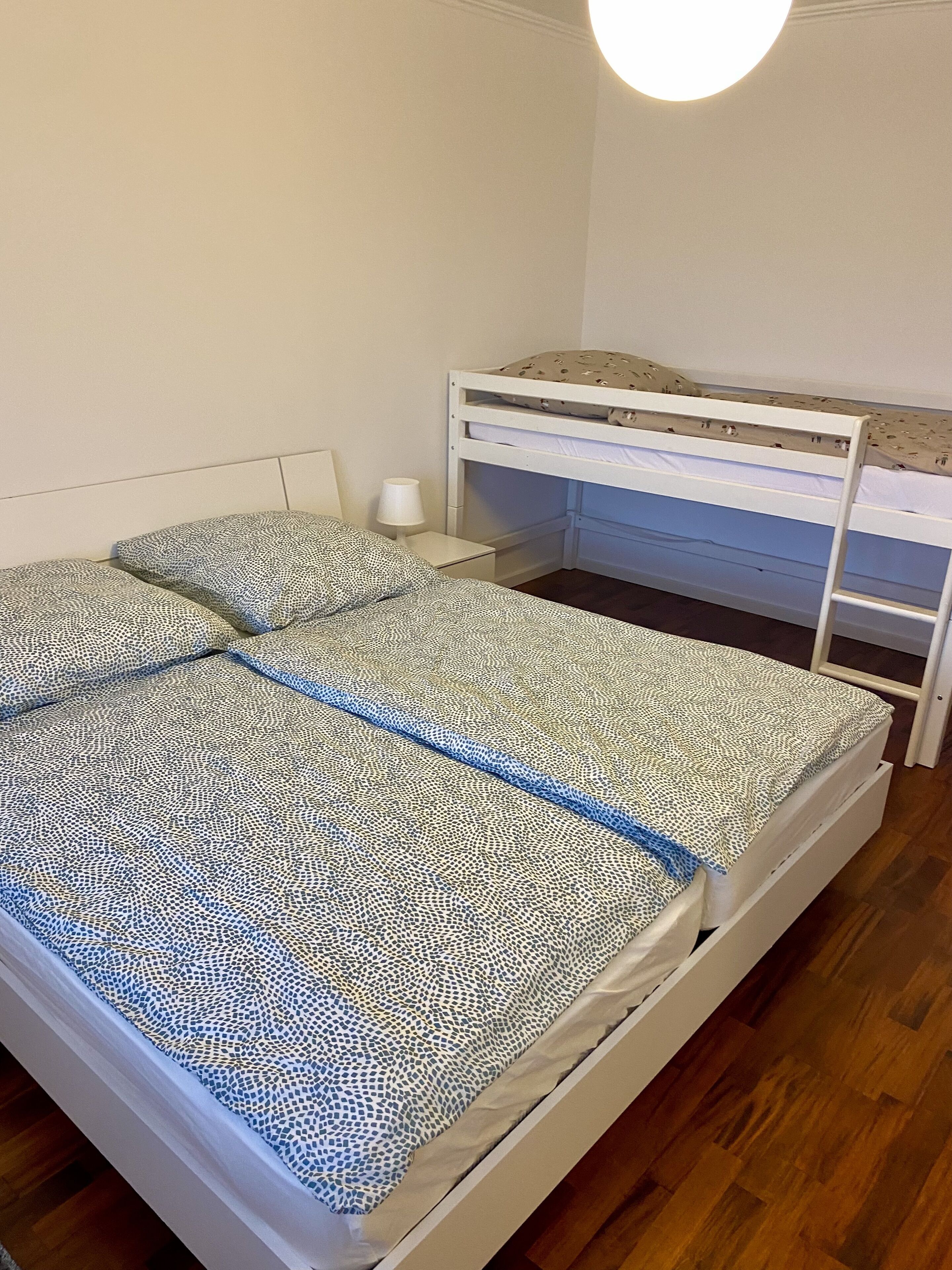 Een slaapkamer met een stapelbed, een nachtkastje met een lamp en een bed met een patroonbeddengoed.