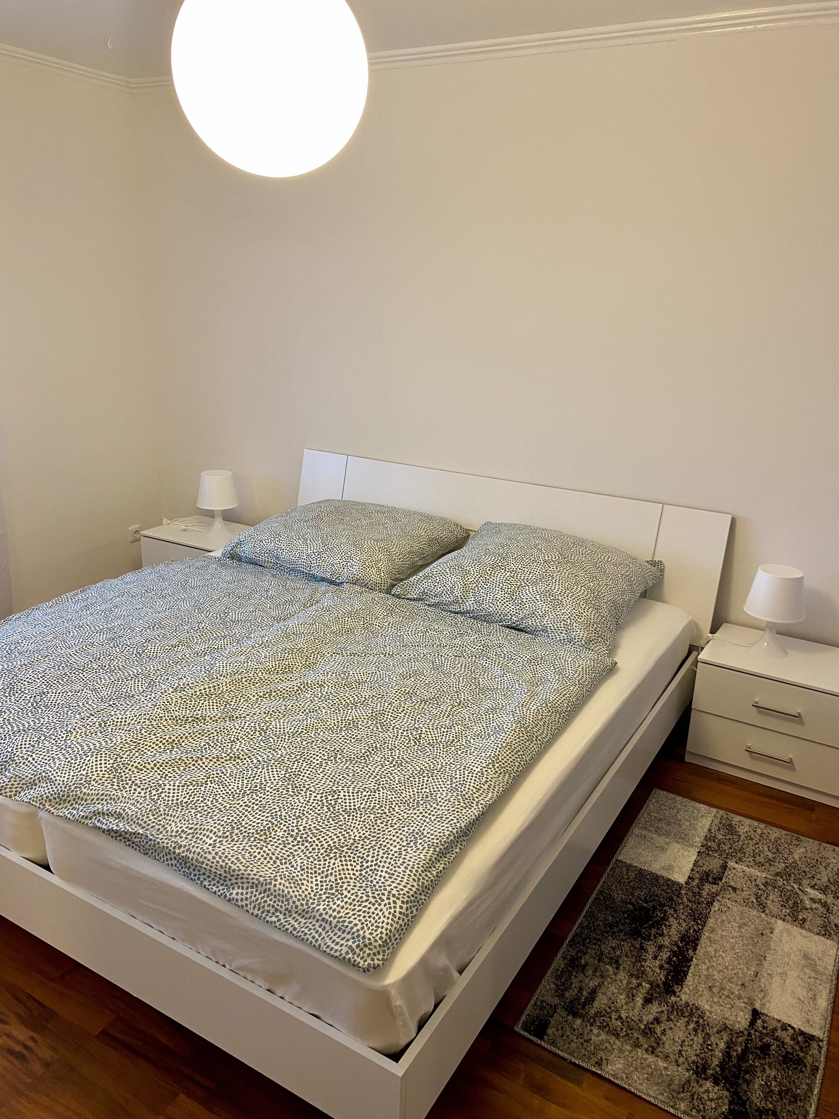 Un lit bien fait, avec une literie à motifs, une table de chevet avec une lampe et un luminaire rond au plafond.