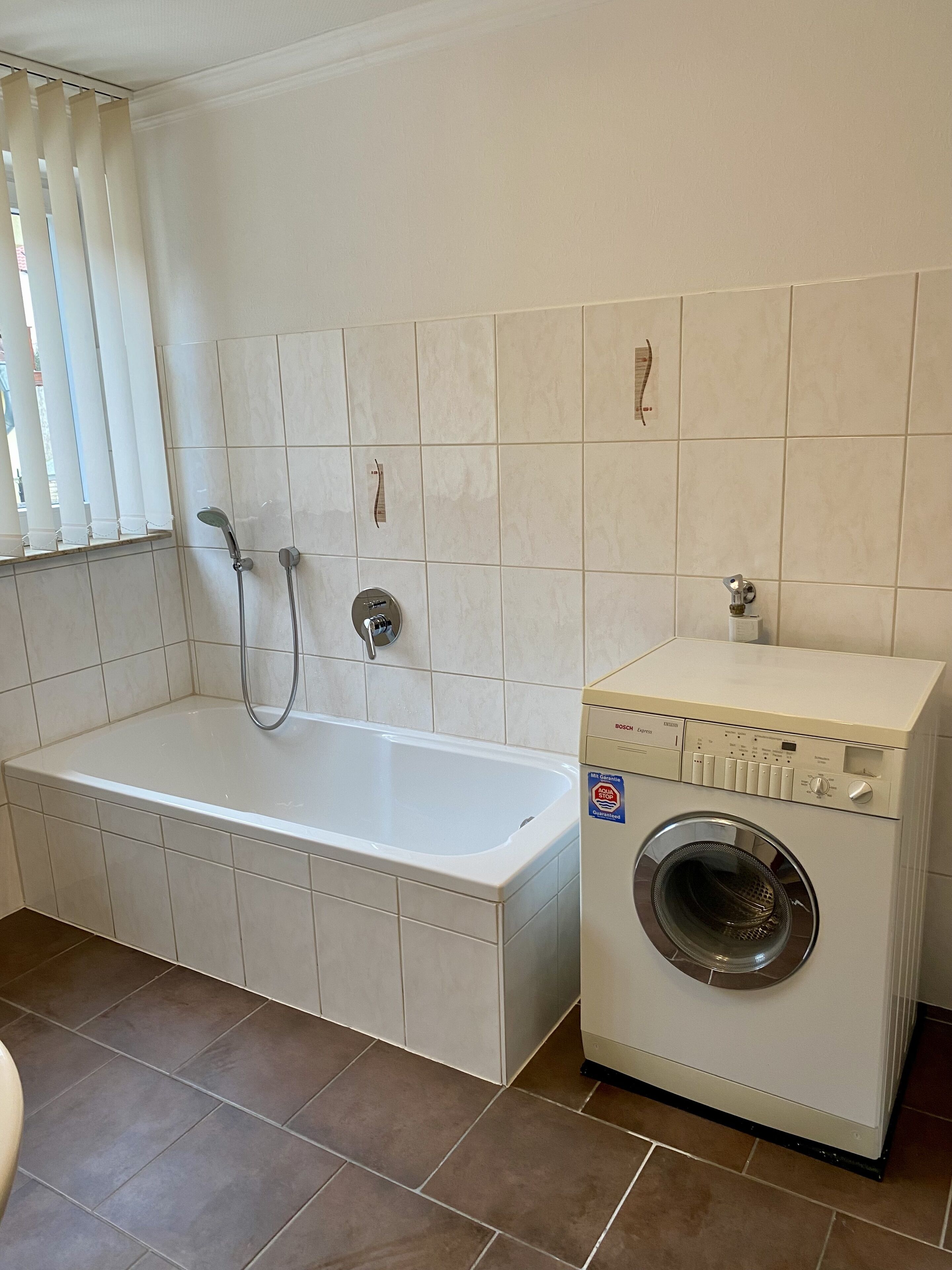 Een badkamer met een badkuip, een douche en een wasmachine met voorlader.