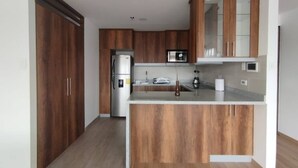 A modern kitchen with wooden cabinets, a stainless steel refrigerator, and a built-in microwave. - Cozy and new Condo. La Carolina 10th floor Unbeatable view.  (Quito)