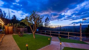 A backyard with a wooden deck, a tree, and a view of the surrounding landscape.