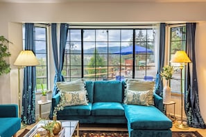 Una habitación con un sofá color turquesa, una mesa de centro, una lámpara y vistas a un paraguas azul y follaje exterior.