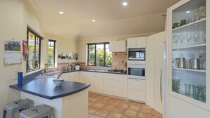 A kitchen with white cabinets, a blue countertop, and a built-in oven. There are two stools and a window with a view of trees. - Jacaranda - Revel in the Panoramic Views (Nelson)