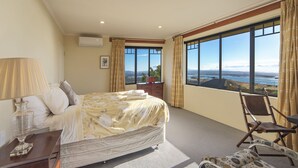 A hotel room with a large bed, a desk, a chair, and a view of the sea. - Jacaranda - Revel in the Panoramic Views (Nelson)