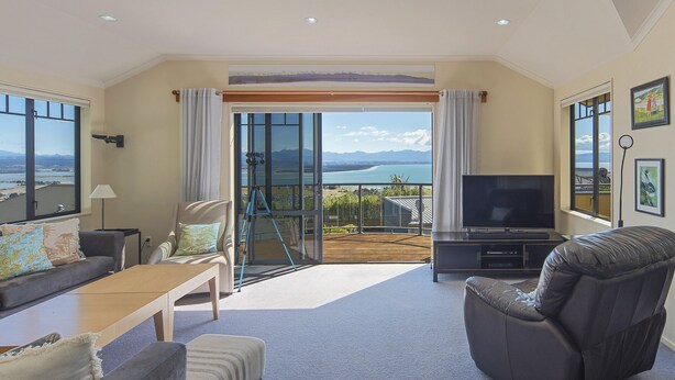 A spacious living room with a large TV, comfortable seating, and a balcony with a scenic view. - Jacaranda - Revel in the Panoramic Views (Nelson)