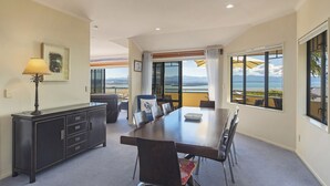 A conference room with a large table, chairs, a desk with a lamp, and a view of the ocean through large windows. - Jacaranda - Revel in the Panoramic Views (Nelson)