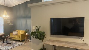 A living room with a yellow sofa, a large flat-screen TV mounted on the wall, a wooden bench, and a potted plant. - Spacious Navarre Home (Navarre)