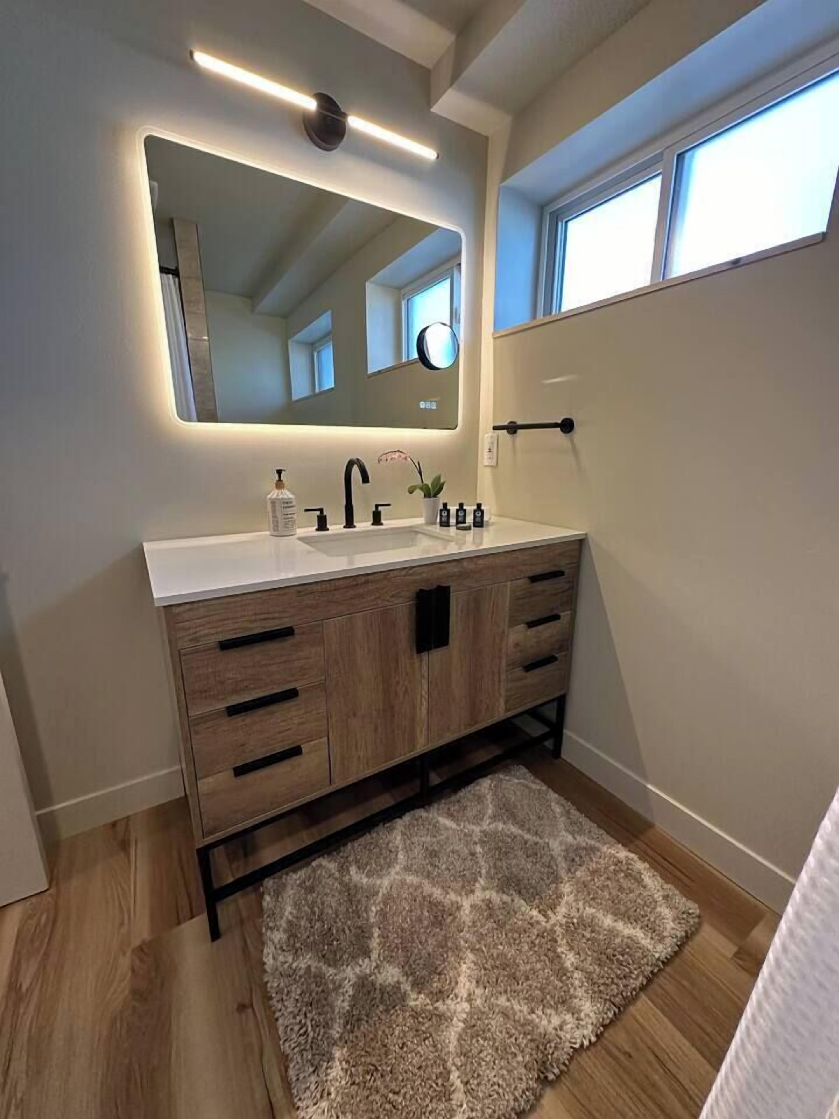 A modern bathroom with a wooden vanity, a large mirror, and a light fixture above the mirror.