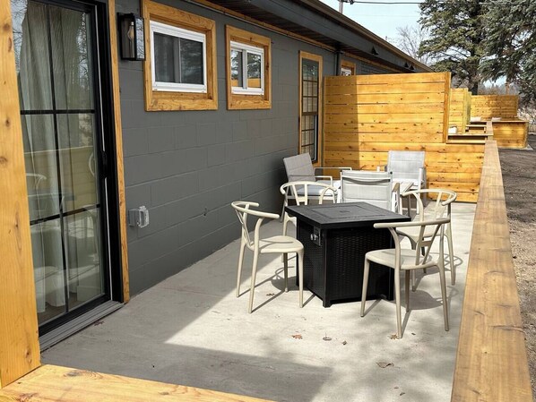 An outdoor patio with a table and chairs, a sliding glass door, and wooden paneling on the walls.