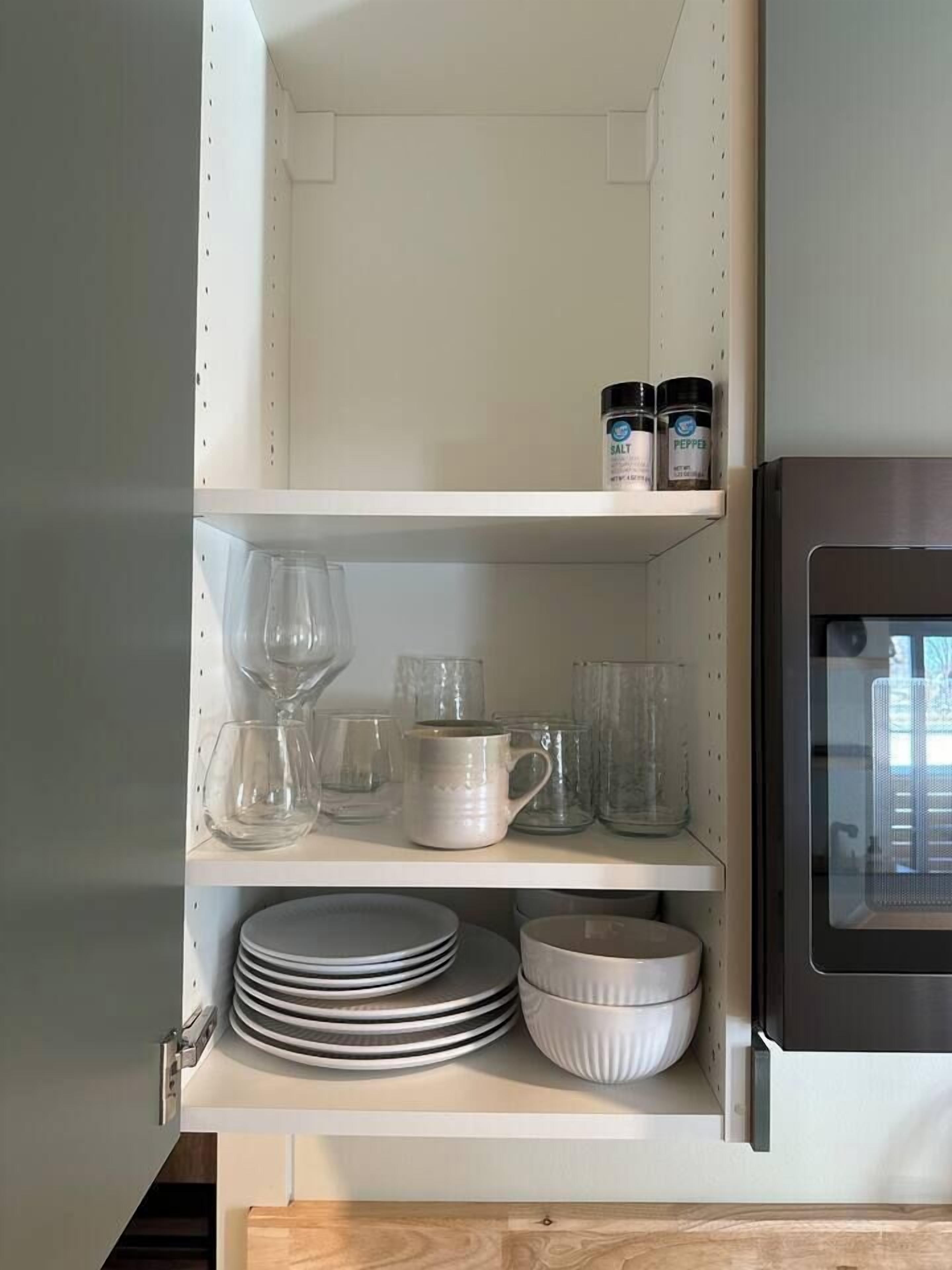 A kitchen with white shelves holding glassware, plates, and a microwave.