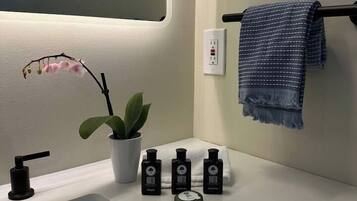 A modern bathroom with a white sink, a mirror, a potted plant, and three bottles of hand soap.