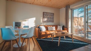 Un salon moderne avec un plafond en bois, une grande fenêtre, un canapé, une table basse et un coin repas comprenant des chaises et une table.
