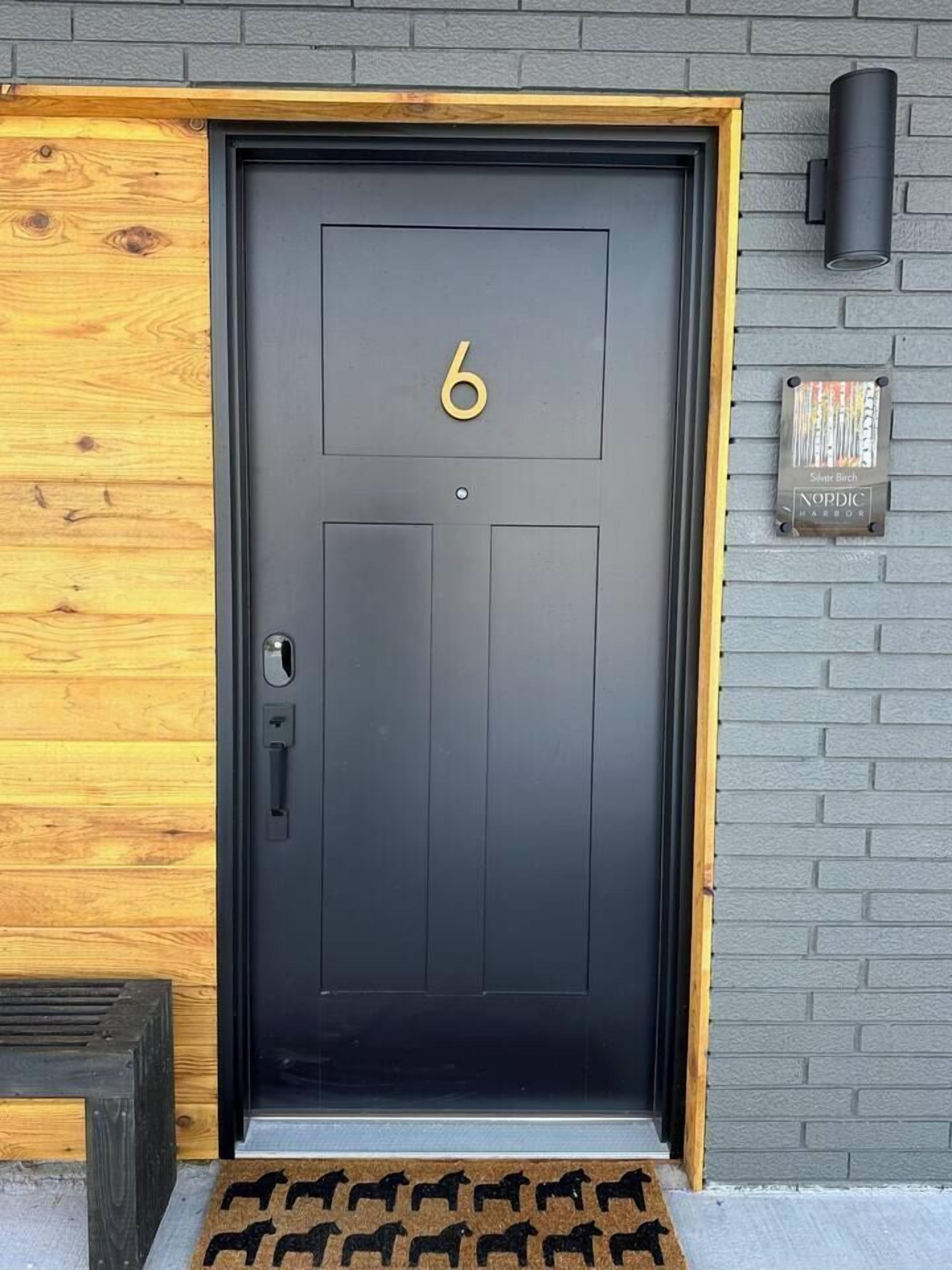 A black door with the number 6, a wooden door frame, a metal handle, and a small plaque on the wall.