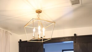 Una stanza con una poltrona grigia, un tappeto decorato, un lampadario e un angolo lavanderia con lavatrice e asciugatrice.