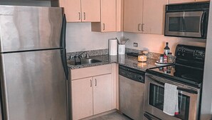 A kitchen with stainless steel appliances, light wood cabinets, a granite countertop, and a black oven. - Beautiful Downtown San Diego Studio (San Diego)