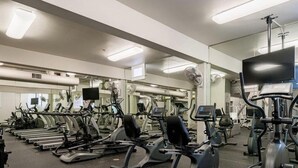 A gym with multiple exercise machines, mirrors, and a large TV screen. - Beautiful Downtown San Diego Studio (San Diego)