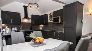 Una cocina moderna con armarios oscuros, una encimera de mármol y un frutero sobre la mesa de comedor.