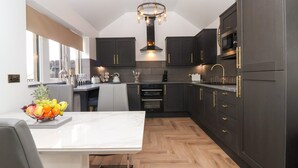 Una cocina moderna con armarios oscuros, encimera de mármol y suelo de parqué.