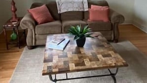 Un salon avec un canapé marron, deux coussins rouges, un plaid à motifs, une table basse en bois ornée d’une plante et une lampe sur une table d’appoint.