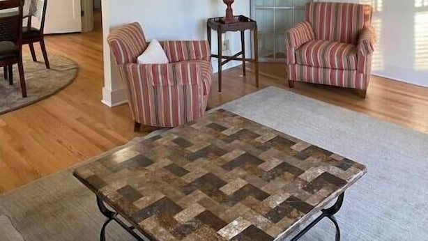 Un salon spacieux doté d’un ventilateur de plafond, de deux fauteuils à rayures, d’une table basse et d’un coin repas avec une table et des chaises en bois.