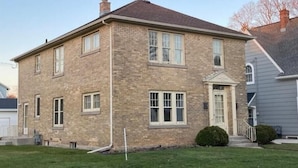 Une maison à deux étages, construite en briques, avec une entrée centrale, un petit porche et une cheminée.