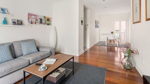 Una sala moderna con un sofá gris, una mesa de centro de madera y un comedor con una mesa y sillas blancas.