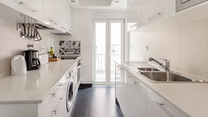 Una cocina moderna con armarios blancos, electrodomésticos de acero inoxidable y un amplio ventanal con vistas a un balcón.