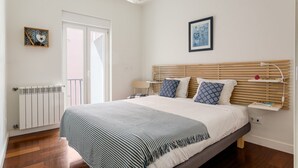 Un dormitorio con cama, mesita de noche, lámpara y una obra de arte en la pared.