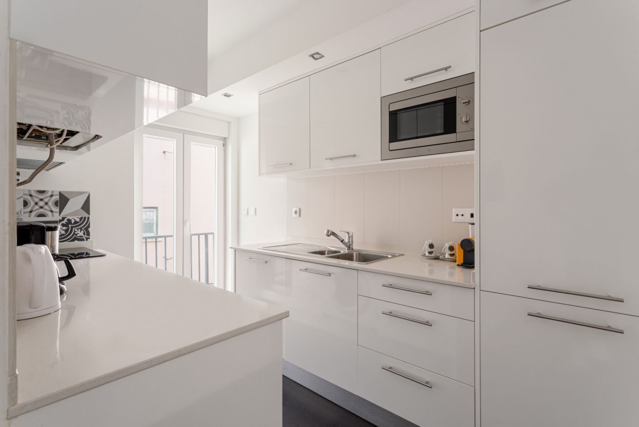 Una cocina moderna con armarios blancos, un lavamanos de acero inoxidable y un microondas.