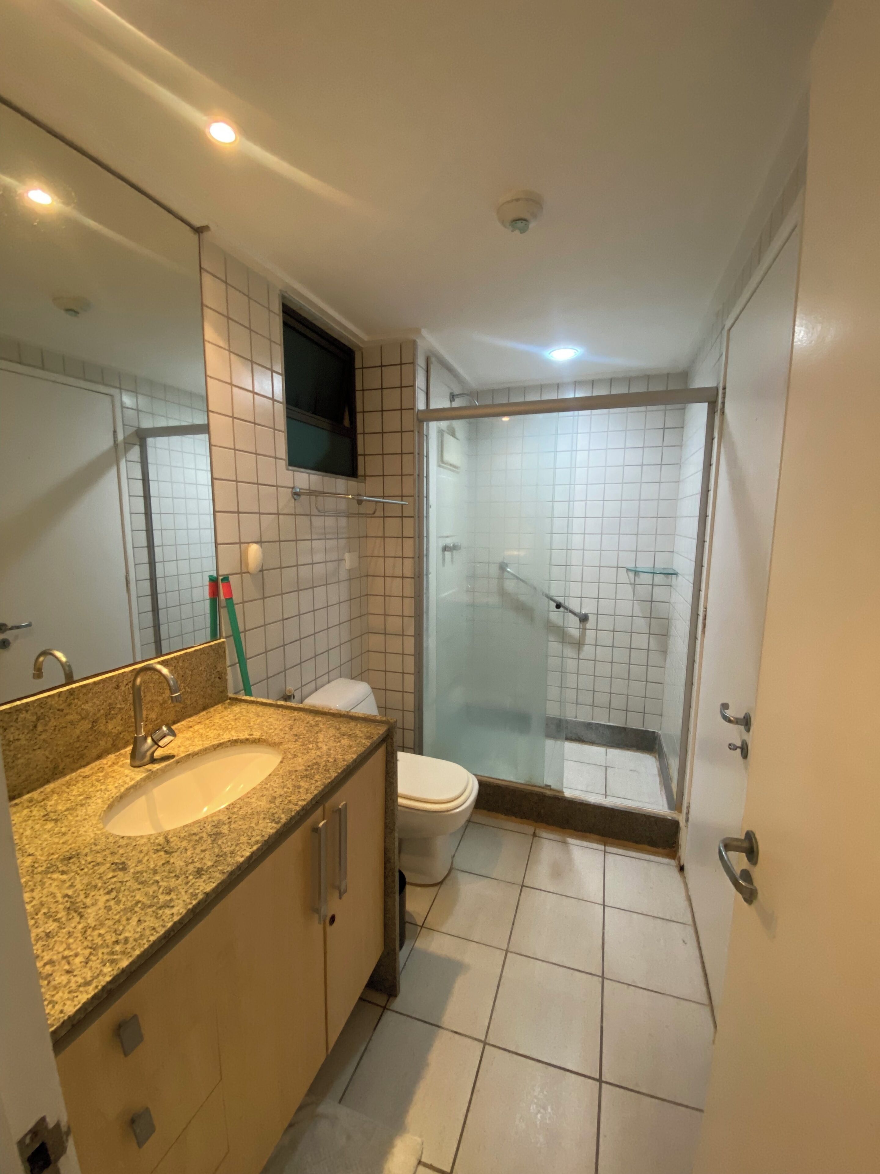 Baño con lavamanos de granito, inodoro y ducha con mampara de vidrio.