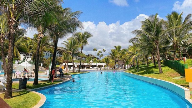 A swimming pool surrounded by palm trees and a building with a white facade. - Flats Beach Class Resort - Muro Alto (Ipojuca)