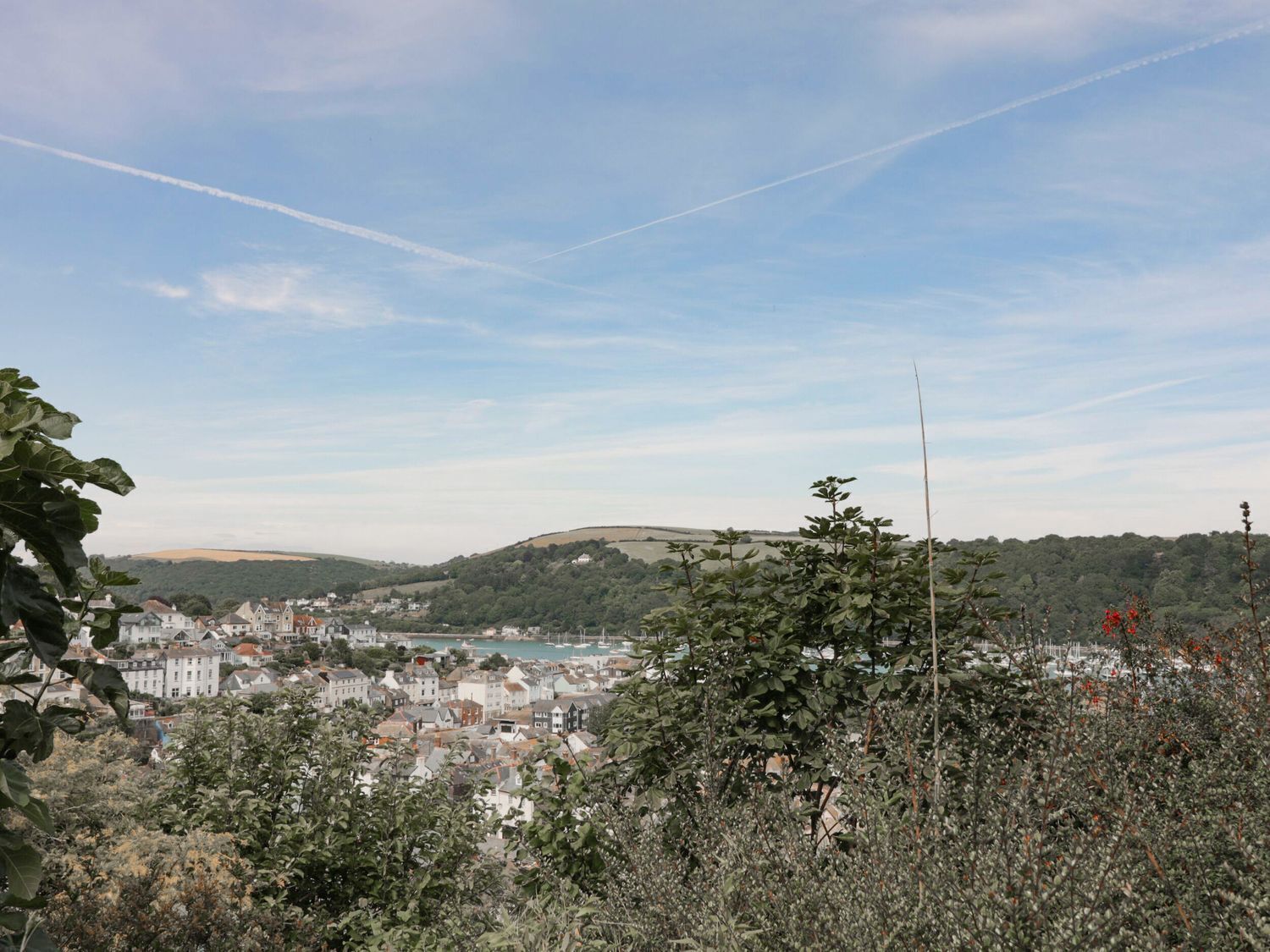 Uma cidade costeira com edifícios ao longo da orla, uma colina ao fundo e céu claro.