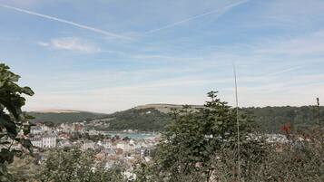 Uma cidade costeira com edifícios ao longo da orla, uma colina ao fundo e céu claro.