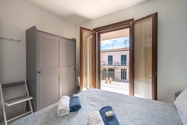 Un dormitorio con cama, armario y balcón con vistas a edificios.