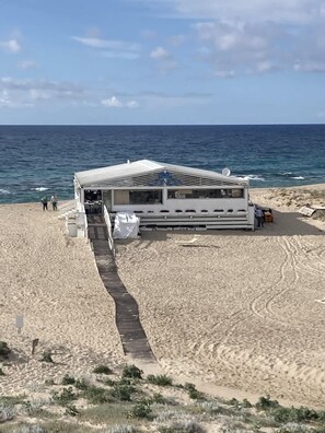 Una casa rodante frente a la playa con un porche cubierto, un sendero arenoso que la lleva a ella, y el océano al fondo.