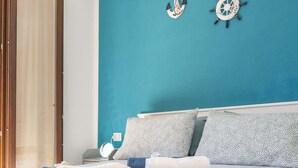A bed with patterned bedding, a nightstand with a lamp, and a wall clock. - Residenza Le Terrazze - Affitti Brevi Italia (Valledoria)
