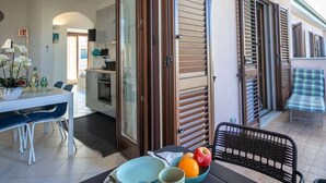 A modern kitchen with a dining area, a balcony with a chair, and a table with fruit. - Residenza Le Terrazze - Affitti Brevi Italia (Valledoria)